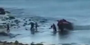 Personas que ayudan a un vehículo atrapado en aguas poco profundas.