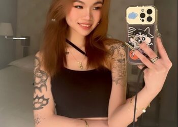 Selfie de una mujer joven con tatuajes y un teléfono.