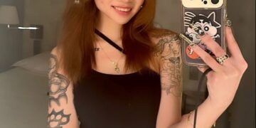 Selfie de una mujer joven con tatuajes y un teléfono.