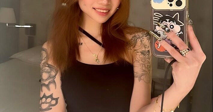 Selfie de una mujer joven con tatuajes y un teléfono.