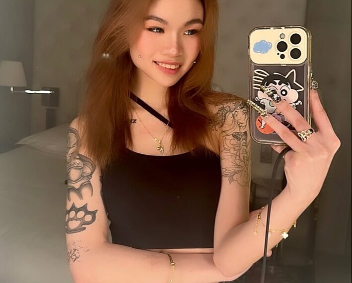 Selfie de una mujer joven con tatuajes y un teléfono.