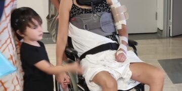 Mujer en silla de ruedas con correa para el cuello y honda de brazo, rodeada de familia.