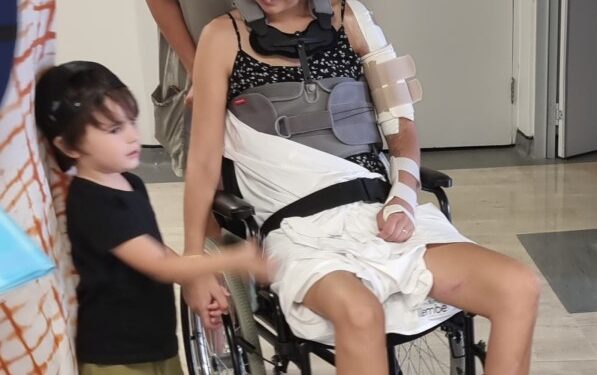 Mujer en silla de ruedas con correa para el cuello y honda de brazo, rodeada de familia.