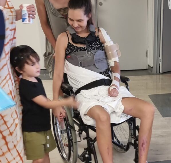 Mujer en silla de ruedas con correa para el cuello y honda de brazo, rodeada de familia.