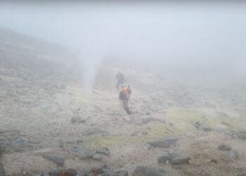 Dos excursionistas que caminan sobre un paisaje volcánico nebuloso.