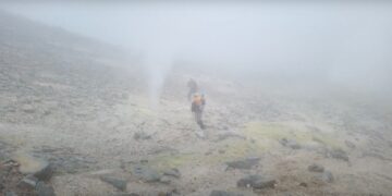 Dos excursionistas que caminan sobre un paisaje volcánico nebuloso.