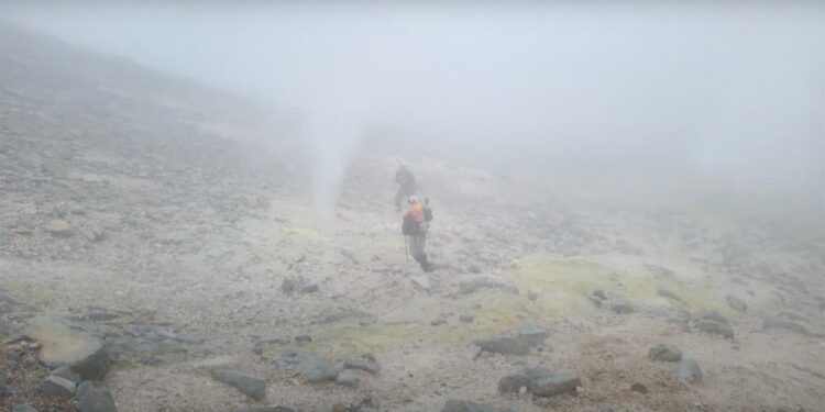 Dos excursionistas que caminan sobre un paisaje volcánico nebuloso.