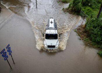 Camión que conduce a través de aguas de inundación en una carretera.