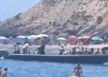Un bote llega a una playa con un gran grupo de personas.