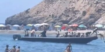 Un bote llega a una playa con un gran grupo de personas.