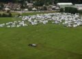Vista aérea de un tractor que extiende el estiércol cerca de numerosas vehículos recreativos estacionados en un campo.