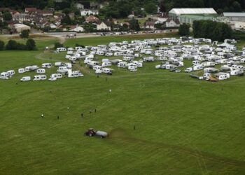 Vista aérea de un tractor que extiende el estiércol cerca de numerosas vehículos recreativos estacionados en un campo.