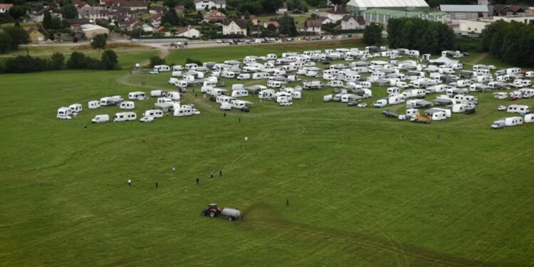Vista aérea de un tractor que extiende el estiércol cerca de numerosas vehículos recreativos estacionados en un campo.
