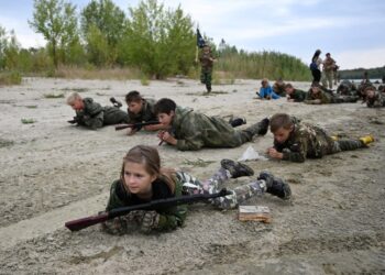 Los estudiantes en uniformes de camuflaje participan en ejercicios de entrenamiento militar.