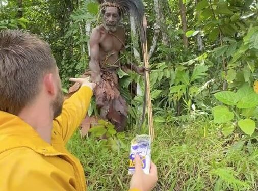 Persona en chaqueta amarilla que ofrece un artículo a la persona indígena en la jungla.