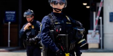 Los oficiales del Departamento de Seguridad Nacional (DHS) se encuentran al guardia frente al Centro de Detención y Detención Federal Edward R. Roybal, mientras que los manifestantes protestan en Los Ángeles el 2 de agosto de 2025. (APU Gomes/Getty Images)