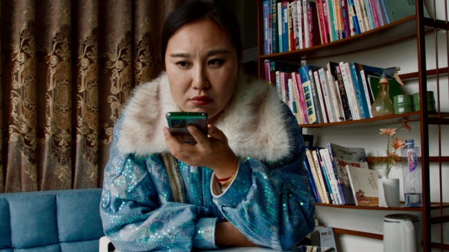 Aún de la película *Mistress Dispeller *, dirigida por Elizabeth Lo. Una mujer usa un teléfono inteligente.