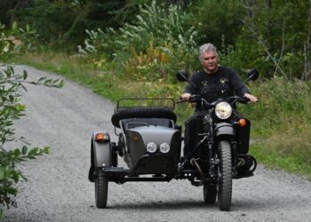 Hombre montando una motocicleta Ural con un sidecar en un camino de grava.