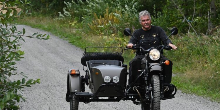 Hombre montando una motocicleta Ural con un sidecar en un camino de grava.