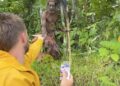 Un hombre con una chaqueta amarilla ofrece un paquete a un hombre de tribus en una jungla.