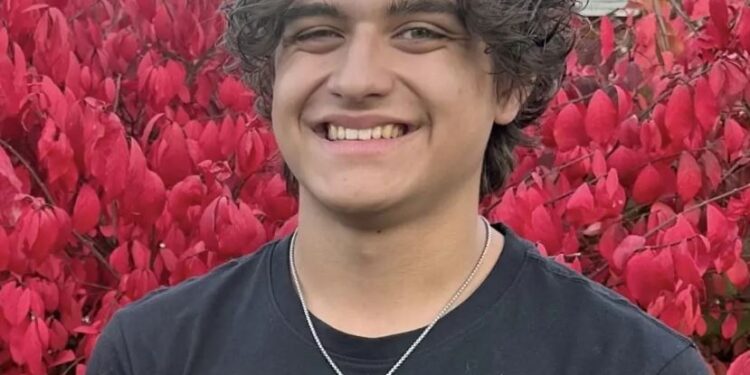 David Nagy, un joven de 17 años, sonriendo, frente a un arbusto de hoja roja.