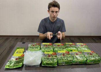 Un hombre con esposas sentado en una mesa con paquetes de metanfetamina de cristal.