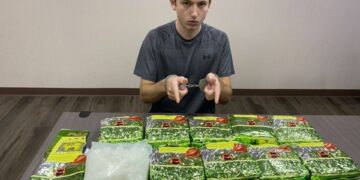 Un hombre con esposas sentado en una mesa con paquetes de metanfetamina de cristal.