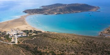 Vista aérea de Prasonisi Beach en Rhodes, Grecia, que muestra un istmo arenoso que conecta una isla de rocas con el continente, con windsurfers y kiteboarders en el agua.