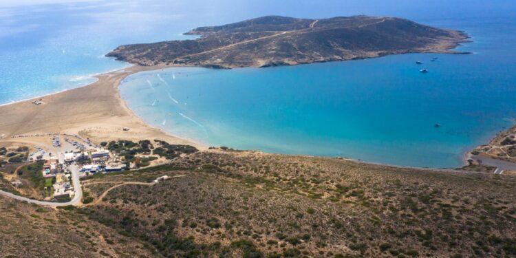 Vista aérea de Prasonisi Beach en Rhodes, Grecia, que muestra un istmo arenoso que conecta una isla de rocas con el continente, con windsurfers y kiteboarders en el agua.
