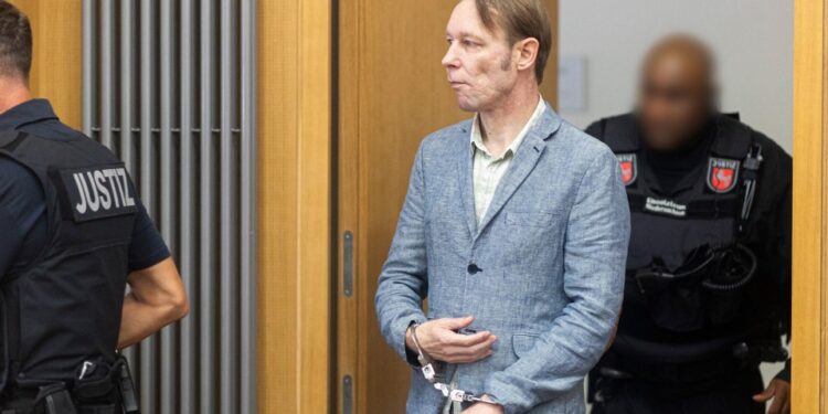 Christian B, con una chaqueta azul claro y esposas, llegando a la corte con guardias.