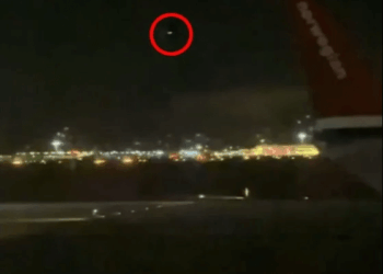 Vista nocturna de un aeropuerto con un círculo rojo que destaca un objeto distante en el cielo.