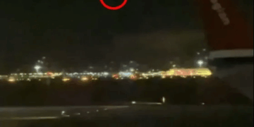 Vista nocturna de un aeropuerto con un círculo rojo que destaca un objeto distante en el cielo.