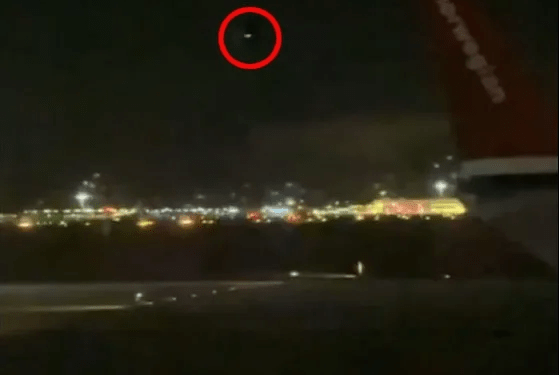Vista nocturna de un aeropuerto con un círculo rojo que destaca un objeto distante en el cielo.