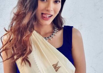 Mujer con una sari de crema y una blusa azul juguetonamente sobresaliendo su lengua.