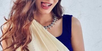 Mujer con una sari de crema y una blusa azul juguetonamente sobresaliendo su lengua.