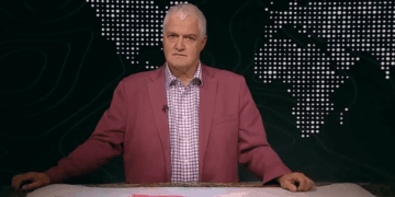 Hombre con una chaqueta rosa que se presenta frente a un mapa mundial.