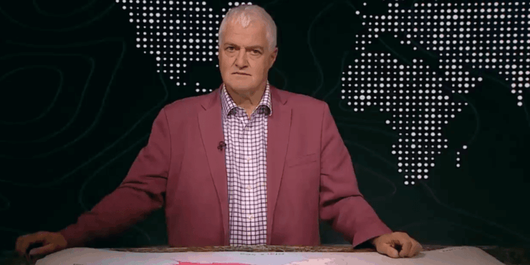 Hombre con una chaqueta rosa que se presenta frente a un mapa mundial.