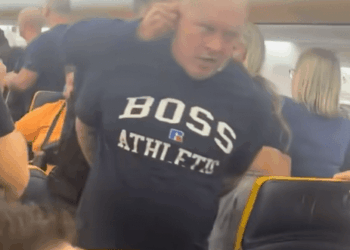 Un hombre con un "Atlético de jefe" Camisa que está restringida en un avión.