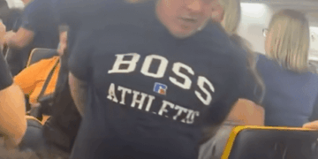 Un hombre con un "Atlético de jefe" Camisa que está restringida en un avión.