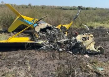 Restos de un avión amarillo en un campo, con tierra quemada y escombros dispersos.
