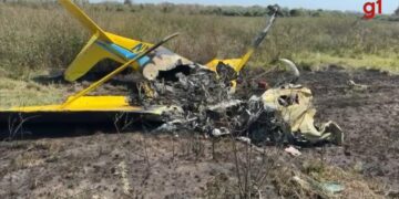 Restos de un avión amarillo en un campo, con tierra quemada y escombros dispersos.