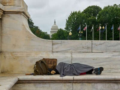 Una persona sin hogar duerme en el banco con el edificio del Capitolio de los Estados Unidos en el fondo.