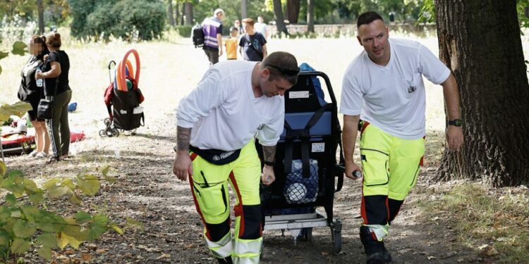 Dos paramédicos llevan a un paciente en una camilla a través de un parque.