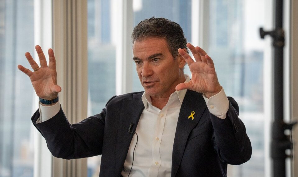 Yossi Cohen, ex jefe de Mossad, con un traje con una cinta amarilla, gestica con ambas manos durante una entrevista.