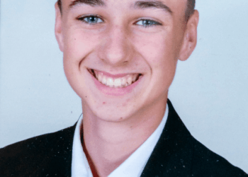 Un joven sonriente con un traje negro y una corbata roja con una camisa blanca.