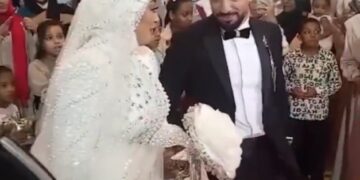 Un novio en un esmoquin sonriendo y sosteniendo la mano de su novia mientras baila en su boda.