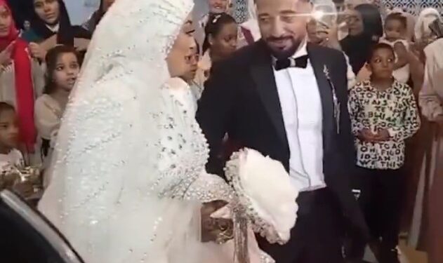 Un novio en un esmoquin sonriendo y sosteniendo la mano de su novia mientras baila en su boda.