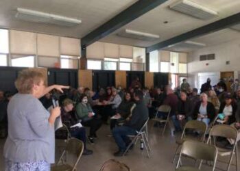Después del incendio de Dixie de 2021, el colectivo de Indian Valley se reúne para su reunión mensual en la cafetería de la Escuela Primaria Greenville, uno de los pocos edificios en Greenville, California, para sobrevivir. Estas reuniones son donde los miembros de la comunidad comparten información vital sobre los esfuerzos de recuperación y los nuevos proyectos. Sue Weber (quien escribió una pieza en advertencia de la bandera roja) está hablando.