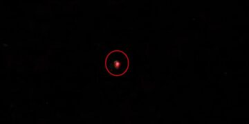 Un pequeño objeto rojo borrosa en el centro de un fondo negro, rodeado en rojo.