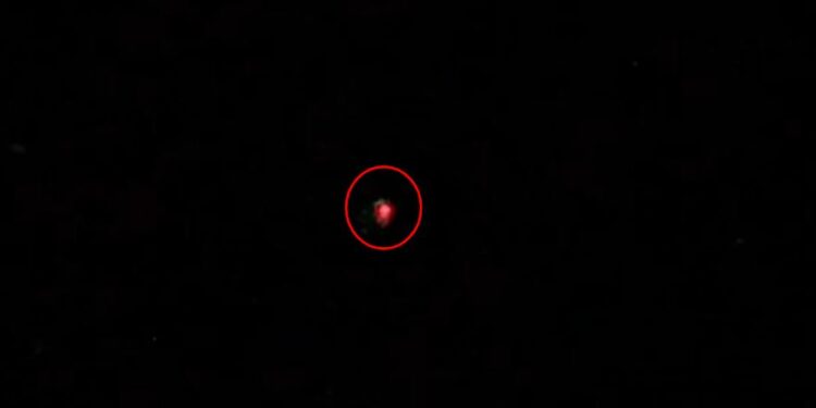 Un pequeño objeto rojo borrosa en el centro de un fondo negro, rodeado en rojo.